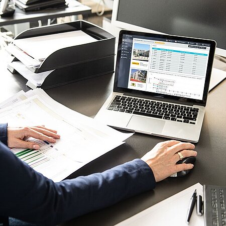 Frau sitzt am Schreibtisch und schaut auf einen Laptop, auf dessen Bildschirm der Energy Monitor von OPTENDA geöffnet ist